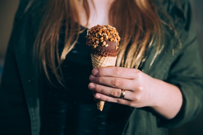 女人在绿色夹克拿着巧克力冰淇淋涂层的坚果白天浅焦点摄影
